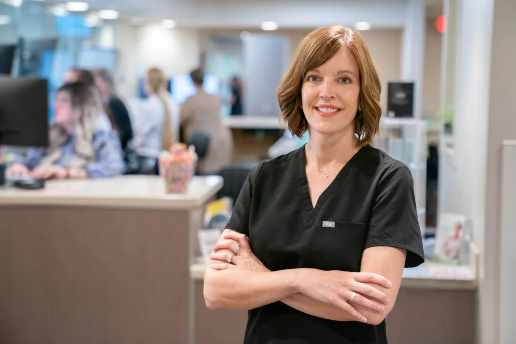 A professional headshot of Dr. Bossenbroek with Southwest Michigan Dermatology's main office front desk in the background.